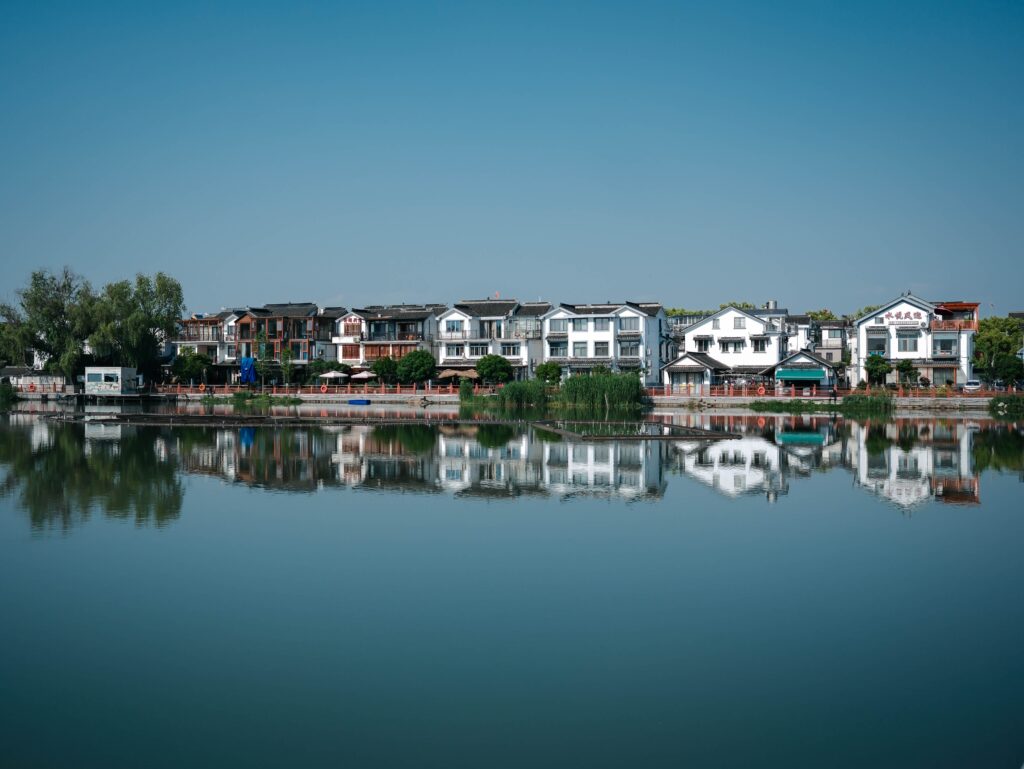 Charming traditional homes reflecting in calm lake waters under a clear blue sky.